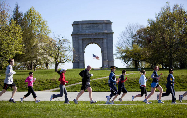 line of people running outdoors with a large concrete archway in the background
